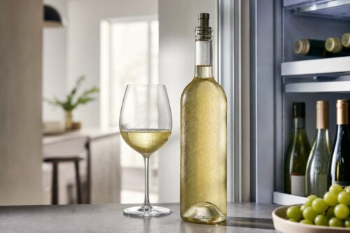Bouteille de vin blanc ouverte et verre servis près d’un réfrigérateur