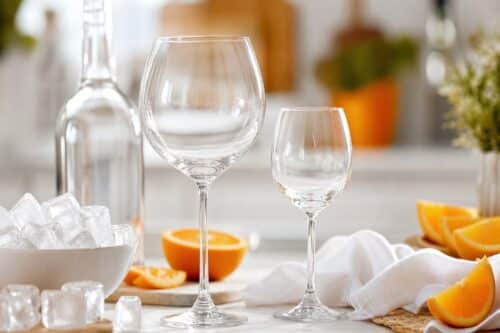 Grand verre ballon et petit verre à pied avec glaçons et oranges sur une table lumineuse