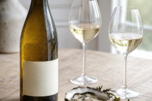 Bouteille de vin blanc à étiquette vierge avec deux verres, huîtres et fromage sur une table