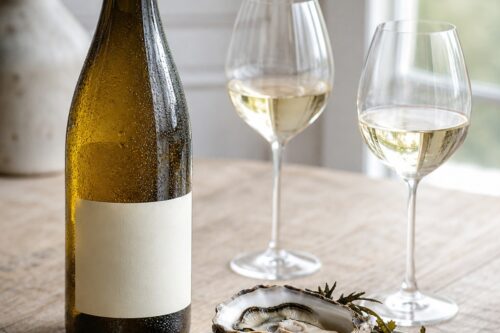 Bouteille de vin blanc à étiquette vierge avec deux verres, huîtres et fromage sur une table