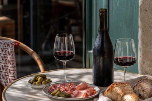 Bouteille de vin rouge sans étiquette avec deux verres, charcuterie et pain sur une table, sans texte ni personne