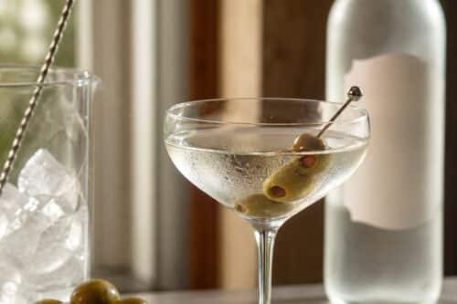 Verre de Dry Martini avec olives, zeste de citron, glaçons et bouteille sans étiquette lisible