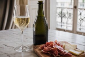 Bouteille de champagne sans étiquette, verre de bulles, jambon cru et comté sur une planche
