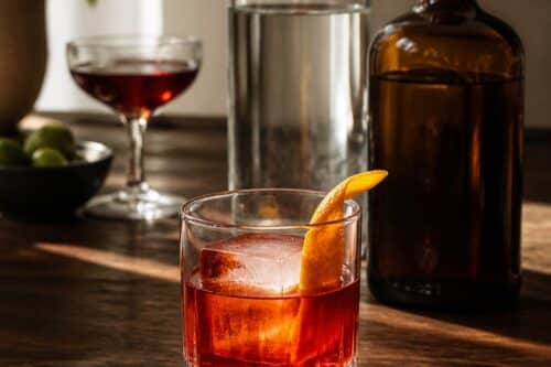 Negroni rouge en verre bas avec un gros glaçon et un zeste d’orange, bouteilles génériques sans étiquette