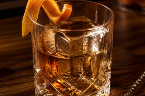Old Fashioned ambré dans un verre bas, gros glaçon carré et zeste d’orange, sans marque ni personne