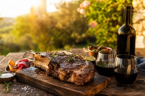 Côte de bœuf grillée sur une table d’été avec bouteille sans étiquette et verres de vin rouge, sans texte ni personne
