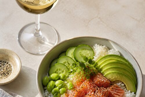 Poke bowl au saumon, avocat, concombre et edamame avec un verre de vin blanc sans marque, sans personne ni texte