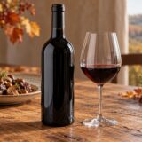Bouteille de vin sans étiquette et verre de vin rouge posés sur une table de repas