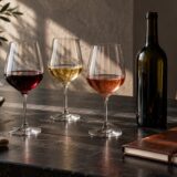 Trois verres à vin et une bouteille sans étiquette sur une table sombre